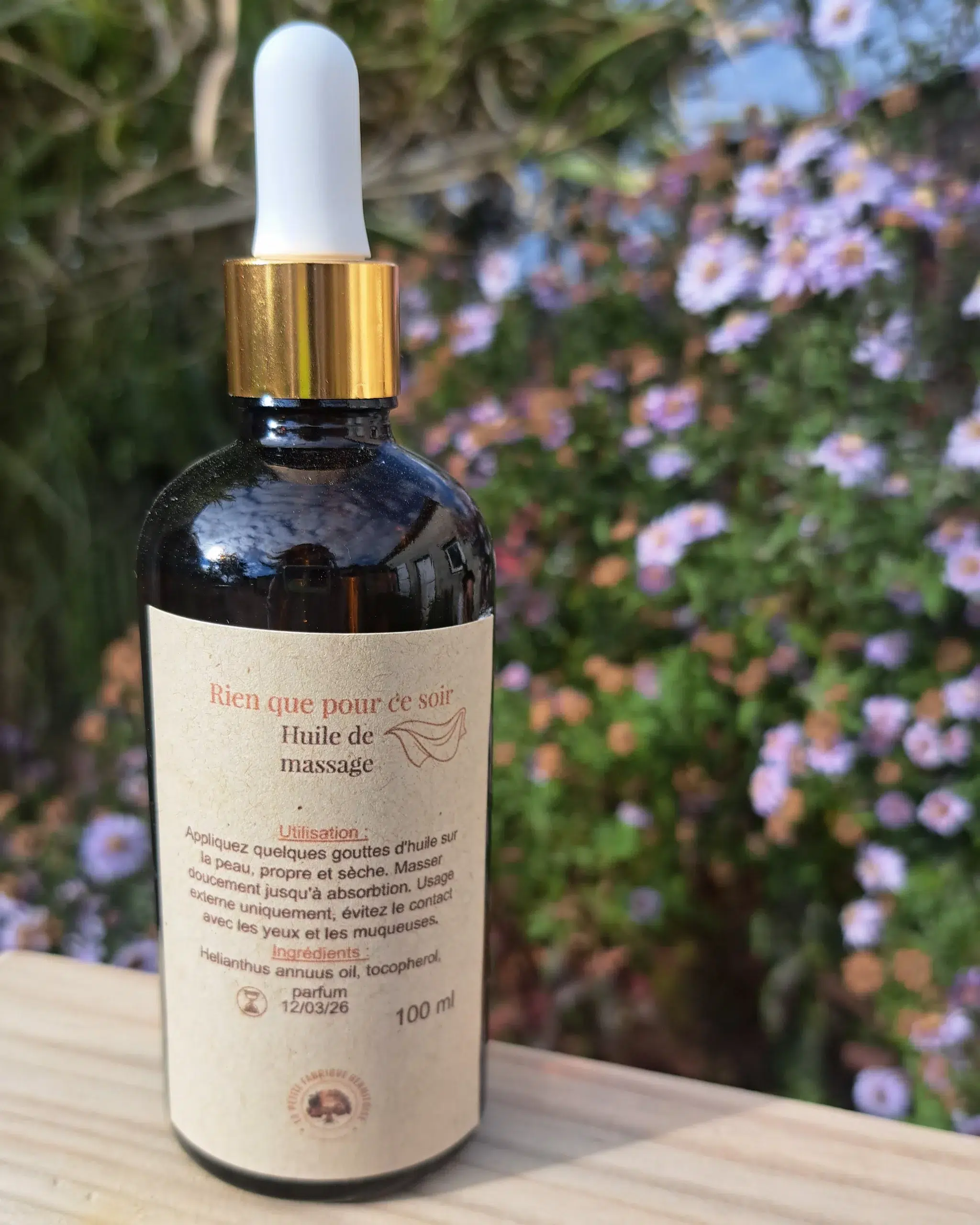 L'huile dans son flacon en verre, sur une planche de bois fond jardin fleuris