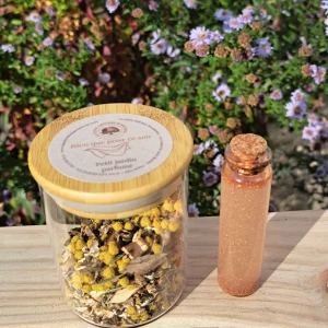 Petit pot en verre transparent contenant les végétaux senteur "Rien que pour ce soir", Sur une planche de bois, fond Jardin fleuris