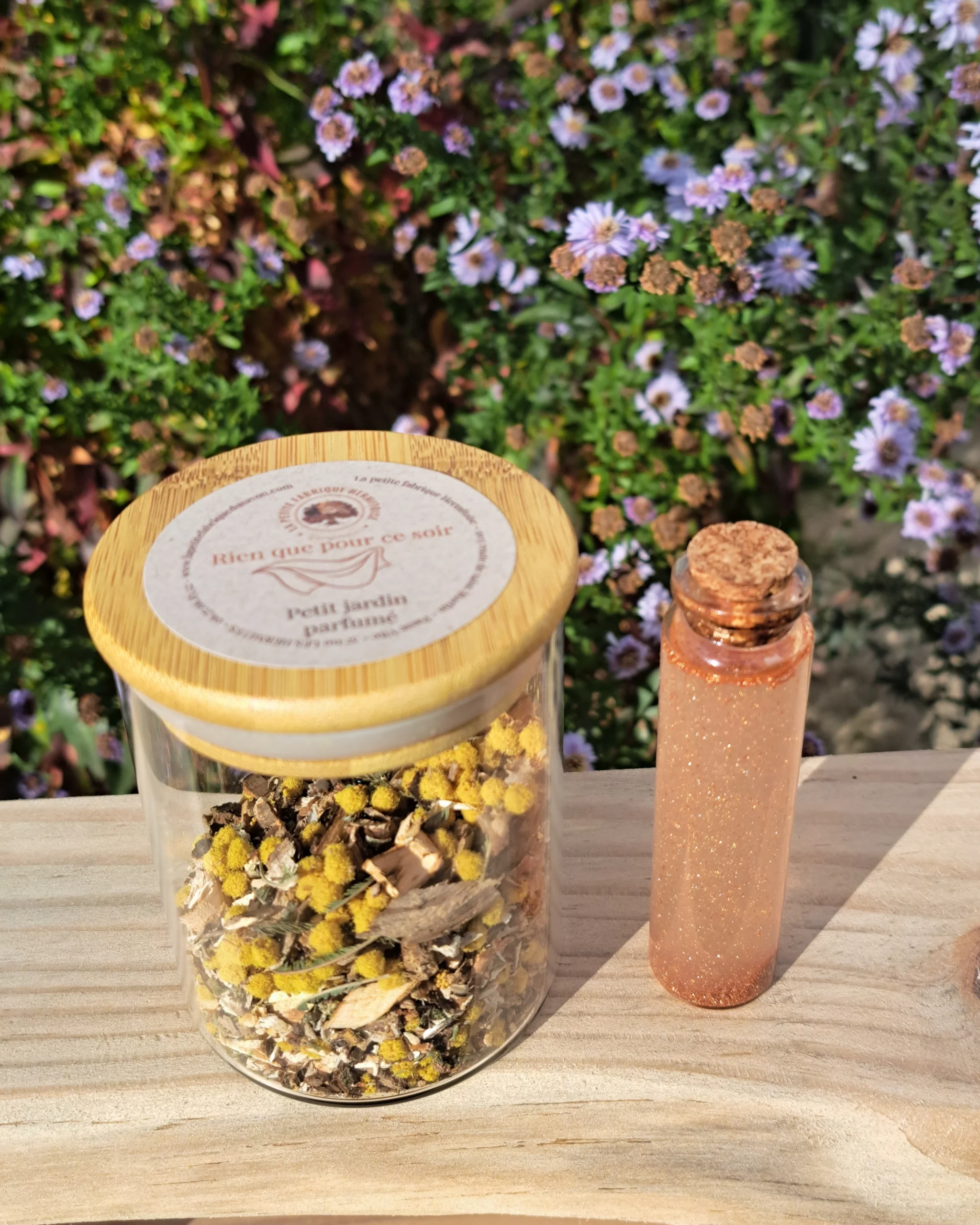 Petit pot en verre transparent contenant les végétaux senteur "Rien que pour ce soir", Sur une planche de bois, fond Jardin fleuris