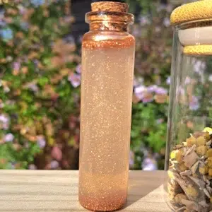 Fiole en verre transparent contenant le parfum. Sur une planche de bois, fond jardin fleuris
