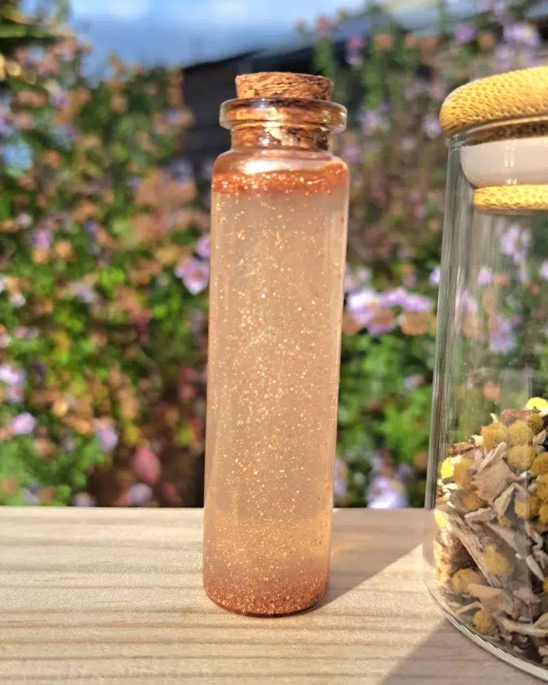 Fiole en verre transparent contenant le parfum. Sur une planche de bois, fond jardin fleuris