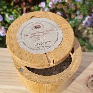 Boite en bambou contenant les sels de bain, sur une planche de bois, fond jardin fleuris