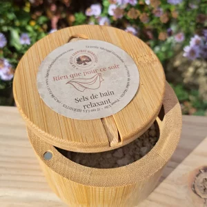 Boite en bambou contenant les sels de bain, sur une planche de bois, fond jardin fleuris